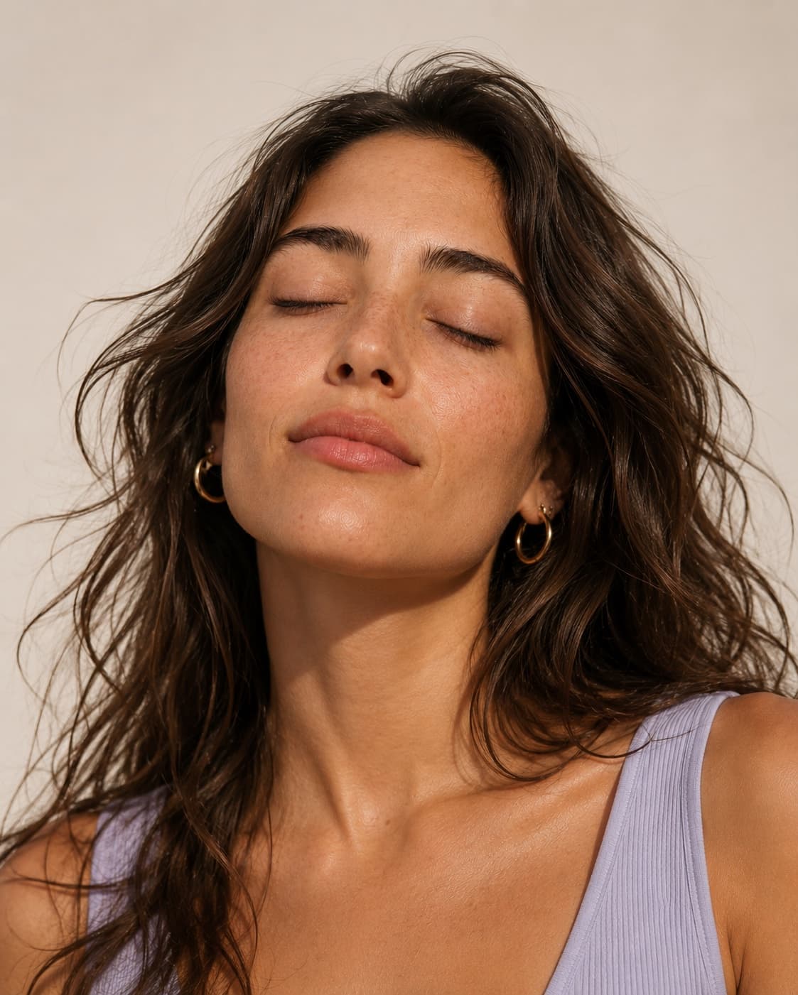 A woman with tousled dark hair, eyes closed, in a lavender top