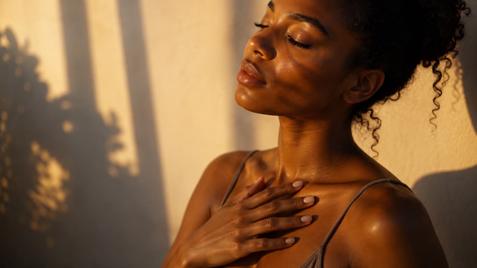 A woman with curly dark hair resting her hand on her chest, eyes closed, in warm evening light