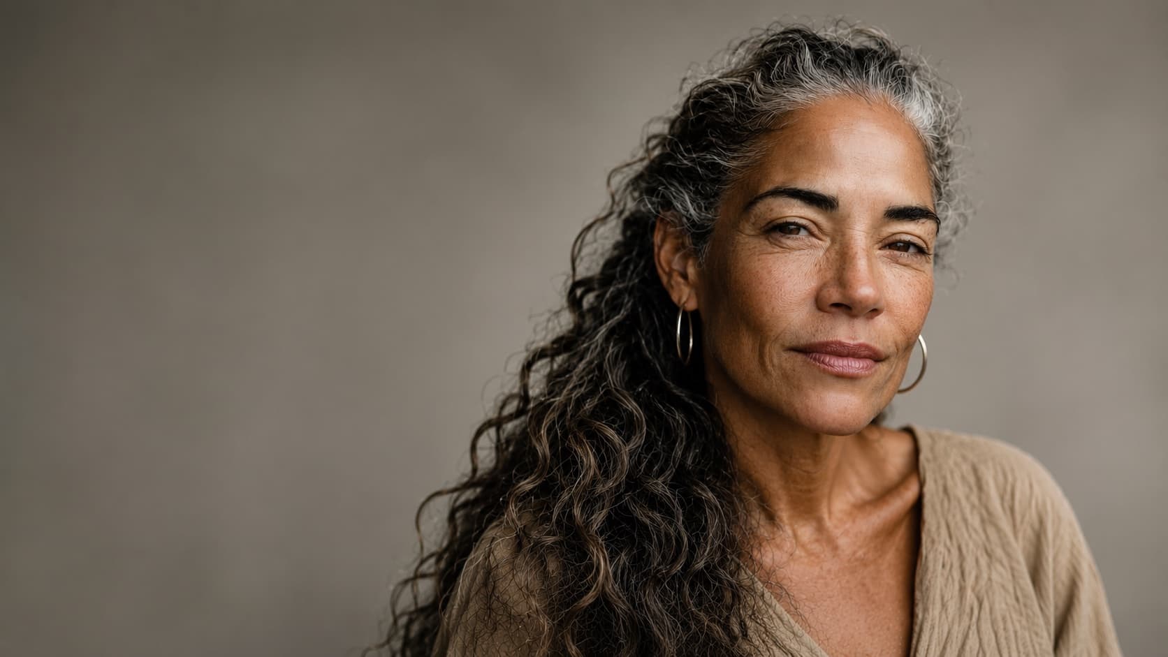 A woman with long curly grey hair and hoop earrings, looking directly at the camera