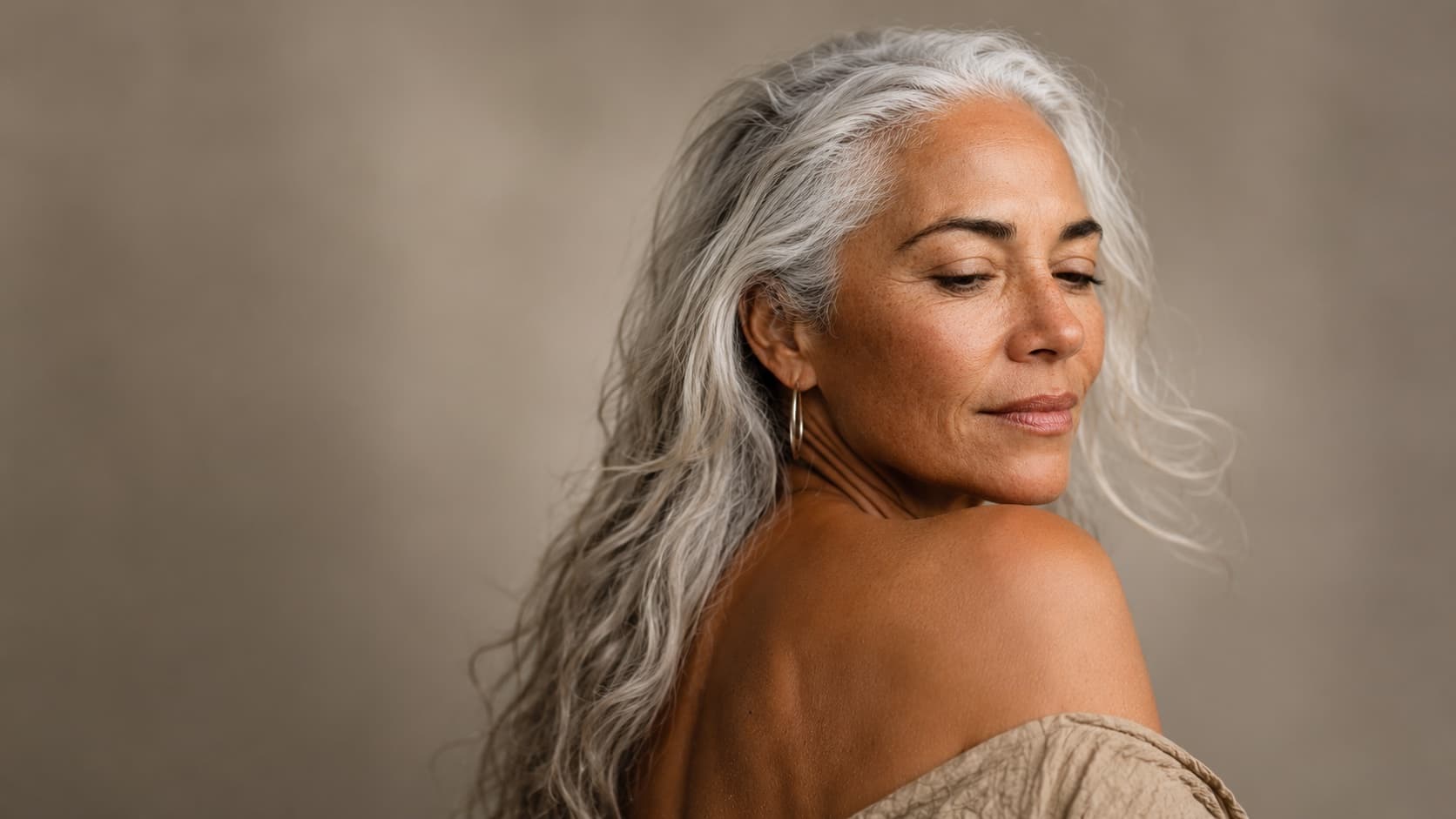 A woman with long grey hair looking back over her bare shoulder