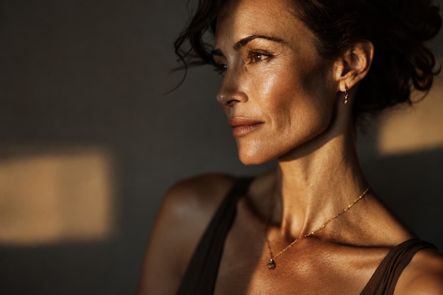 A woman with dark wavy hair looking off to the side, lit by warm side light