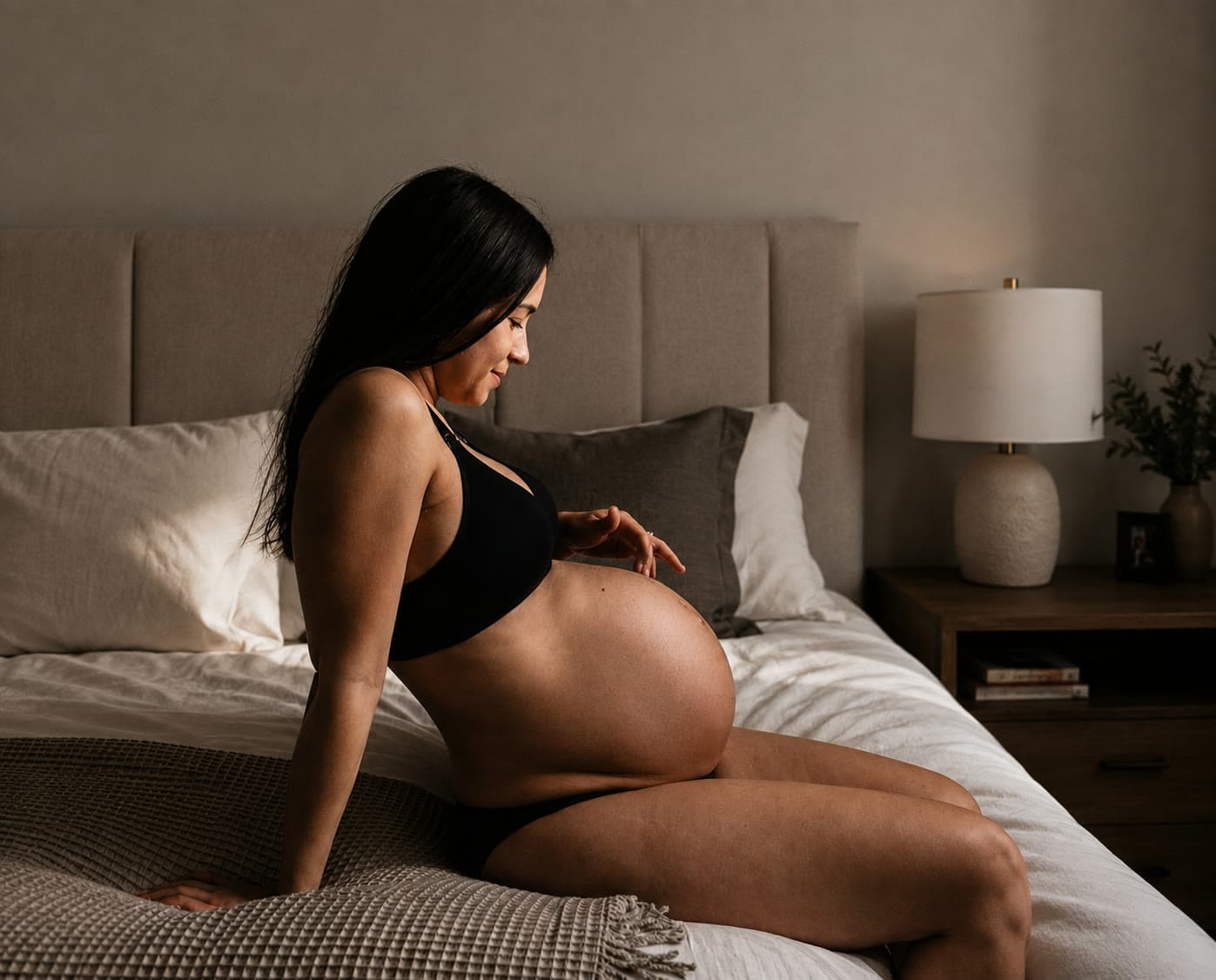 A pregnant woman sitting on the edge of a bed